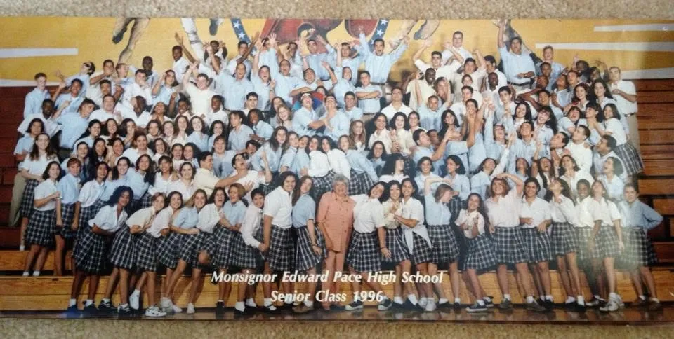 The Pace senior class of 1996 packed onto the gym bleachers in uniform, arms up, with "Monsignor Edward Pace High School, Senior Class 1996" printed across the bottom