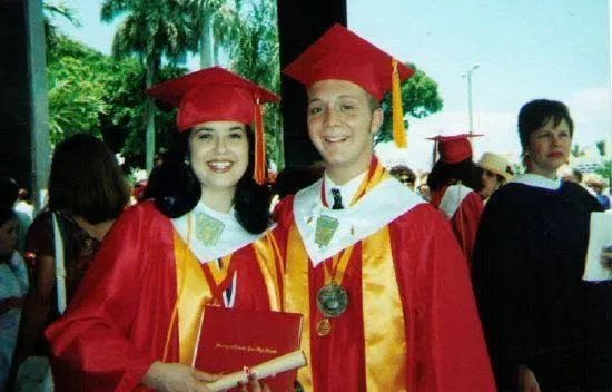 Two graduates in red caps and gowns, diploma in hand