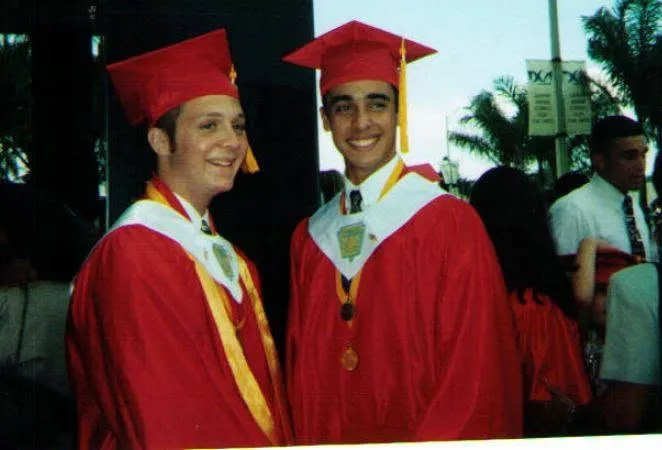 Two graduates in red caps and gowns under the palm trees